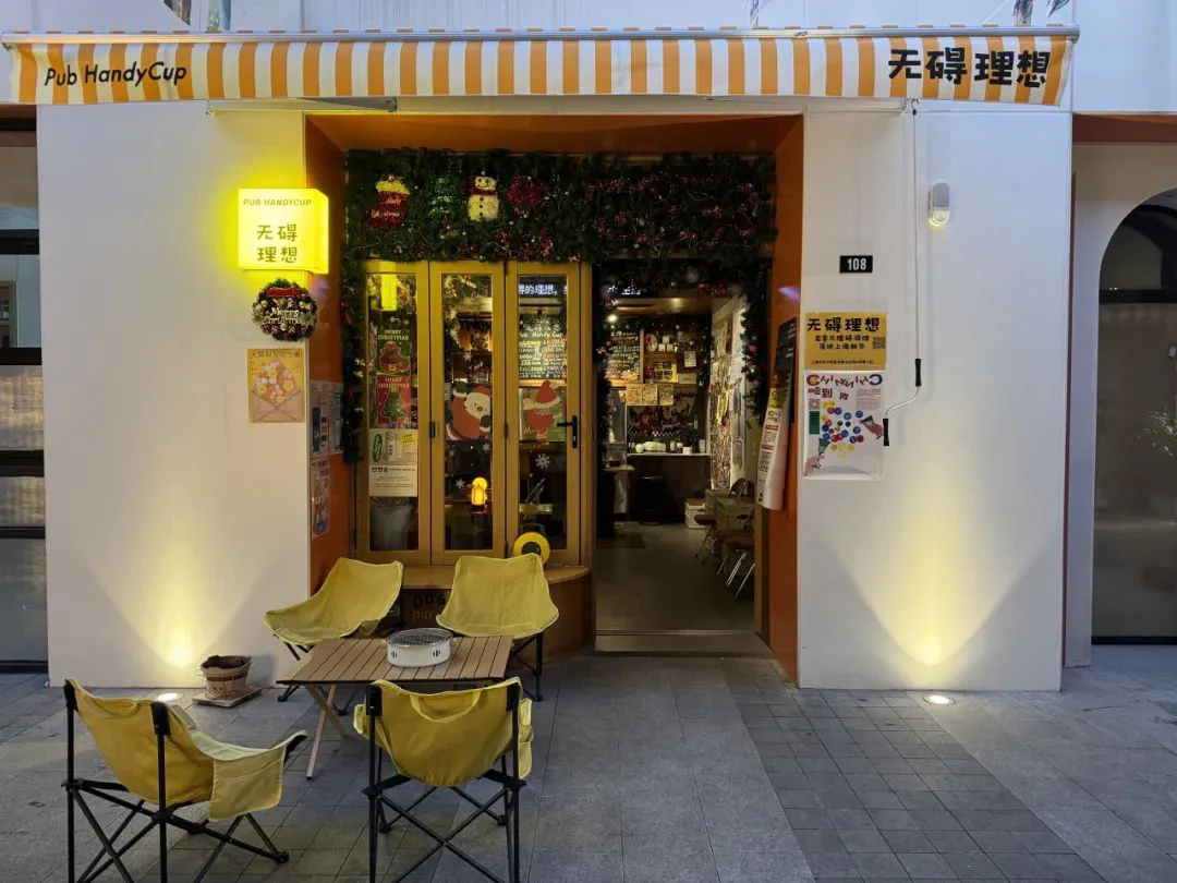 The entrance of Pub HandyCup, with a yellow and white striped awning and outdoor seating.